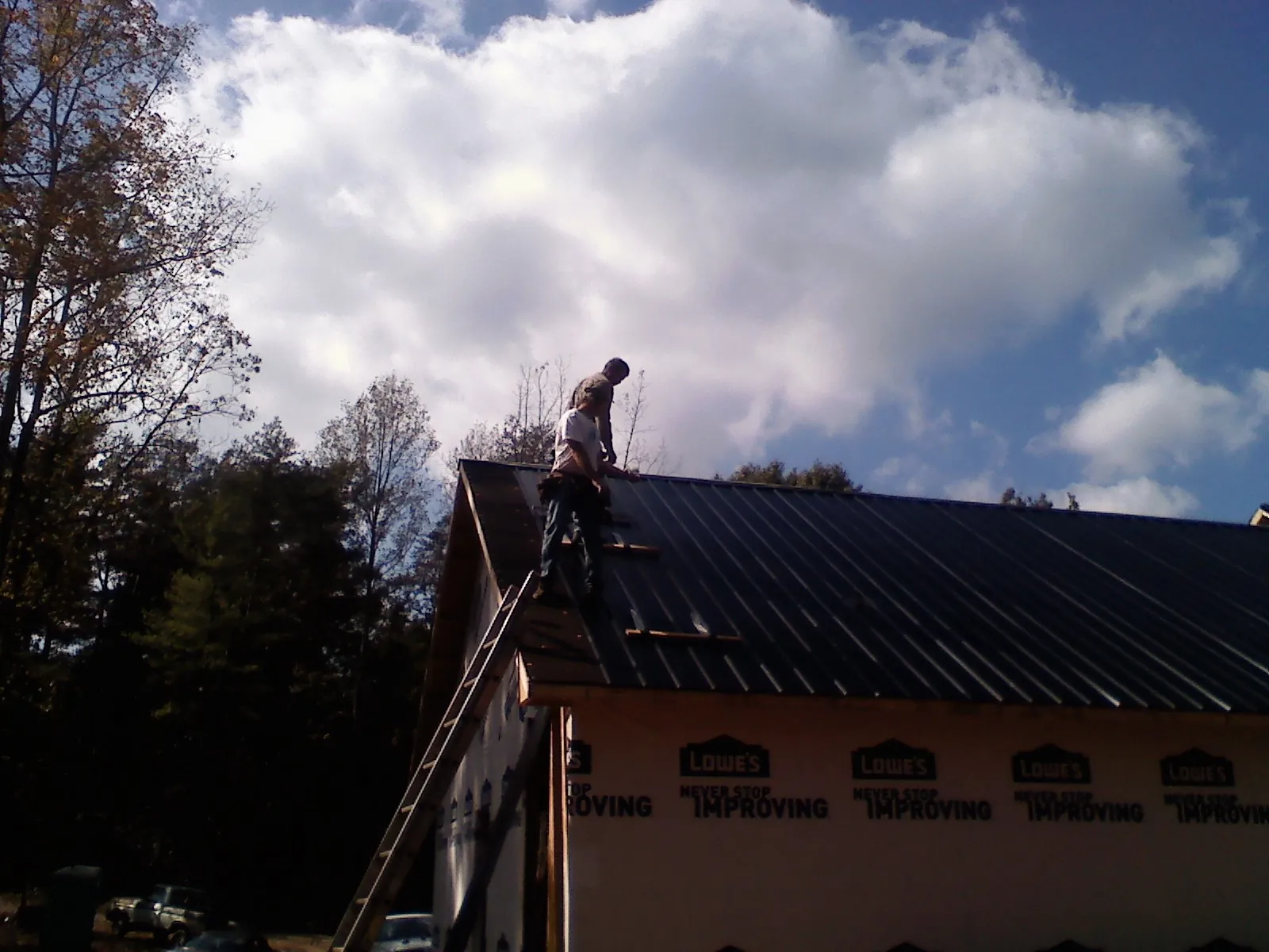 Roofer fastening dark metal panels high against a cloudy sky, from a Roof Inspection job in Willimantic